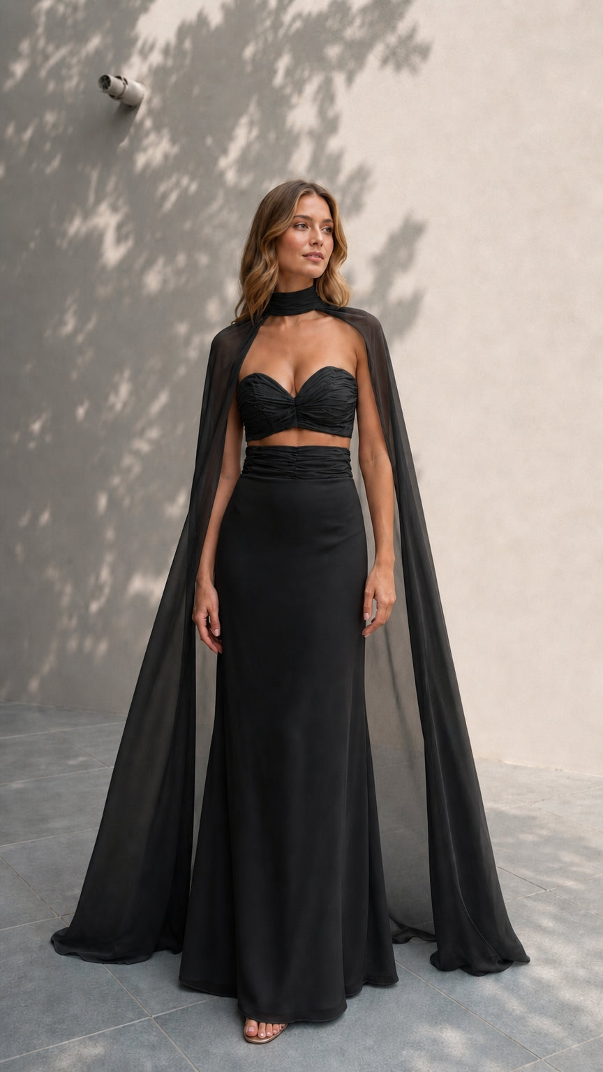 Model wearing elegant black two-piece gown with matching black cape
