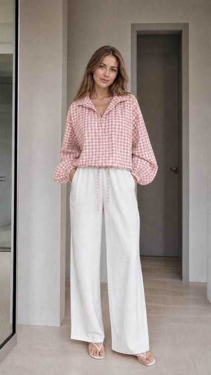 Woman wearing pink gingham check blouse and white wide-leg trousers, front view