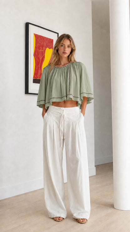 Front view of sage green embroidered cropped swing top styled with linen trousers