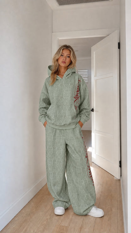 Model wearing sage green embossed monogram hoodie and wide-leg tracksuit set