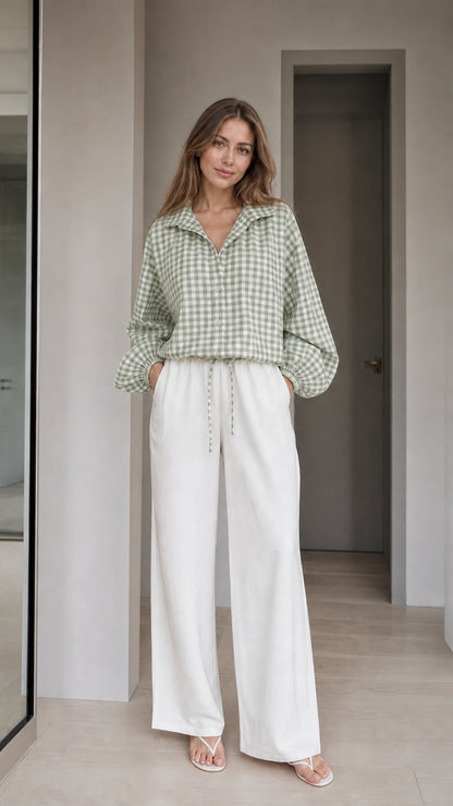 Woman wearing sage green gingham check blouse and white wide-leg trousers, front view