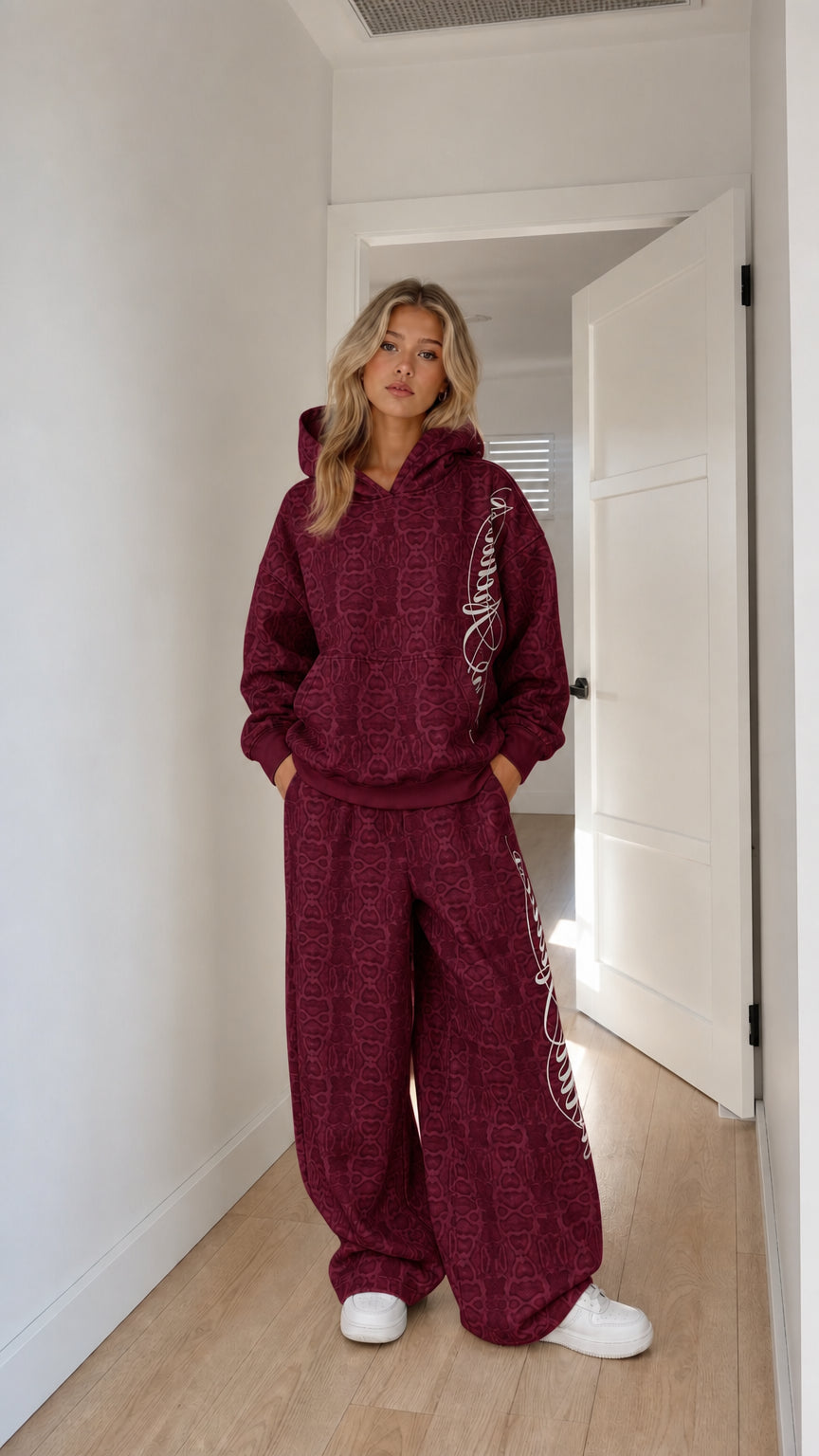 Model wearing burgundy embossed monogram hoodie and wide-leg tracksuit set