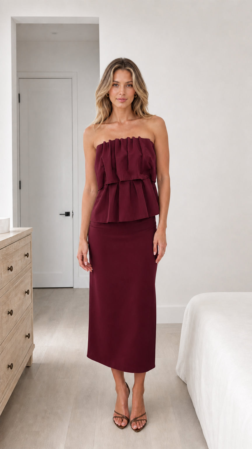 Front view of model wearing burgundy strapless ruffle top and midi skirt set