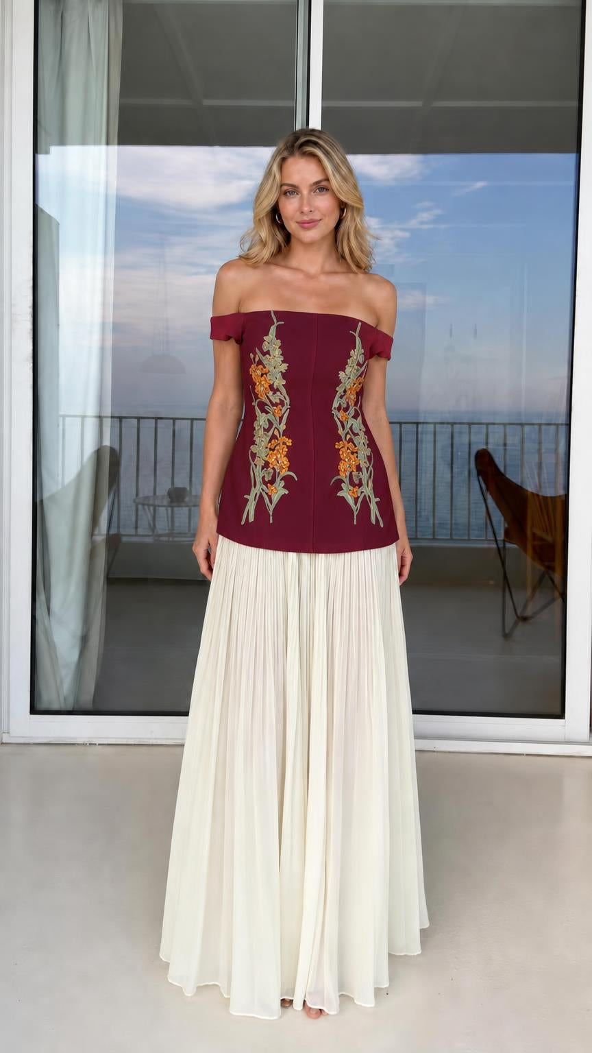 Model wearing burgundy off-shoulder floral embroidered top with white pleated skirt