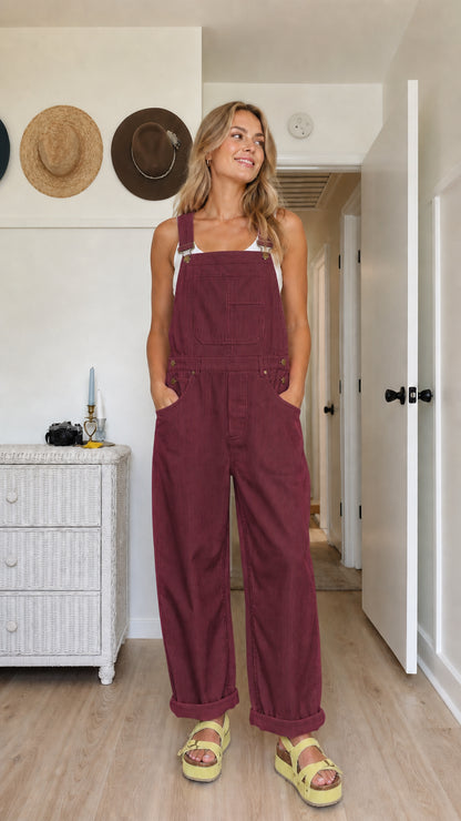 Model wearing burgundy wide-leg bib overalls with adjustable straps and a front bib pocket