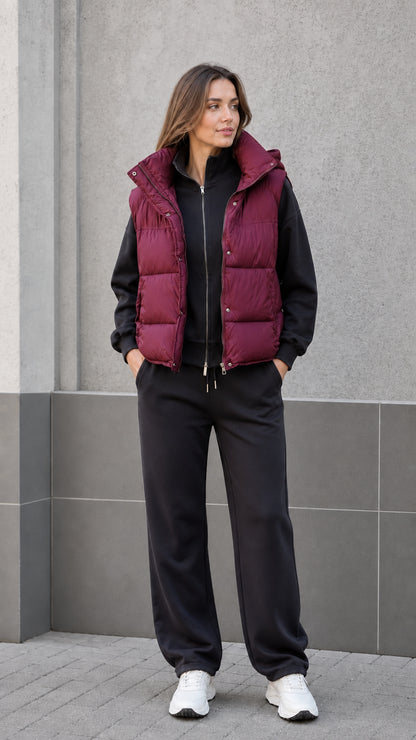 Front view of woman wearing burgundy hooded puffer vest with black sweatsuit