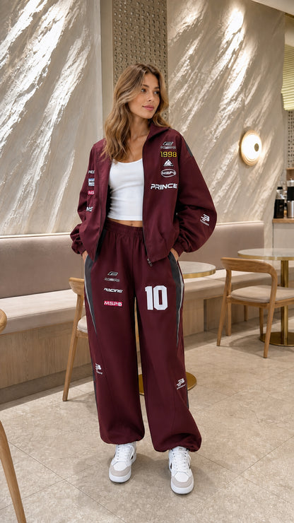 Model wearing burgundy red graphic racing tracksuit set with white sneakers