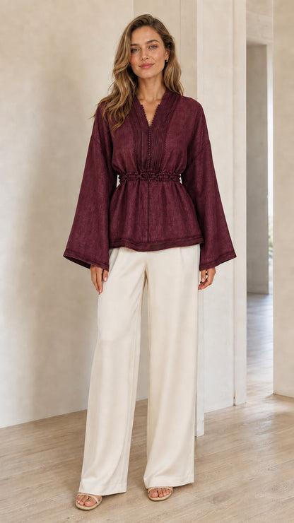 Model wearing burgundy wine red peplum blouse with bell sleeves and trim accents