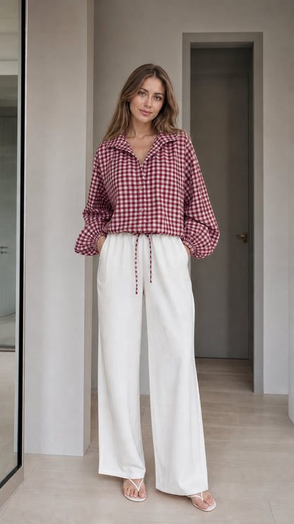 Woman wearing burgundy gingham check blouse and white wide-leg trousers, front view