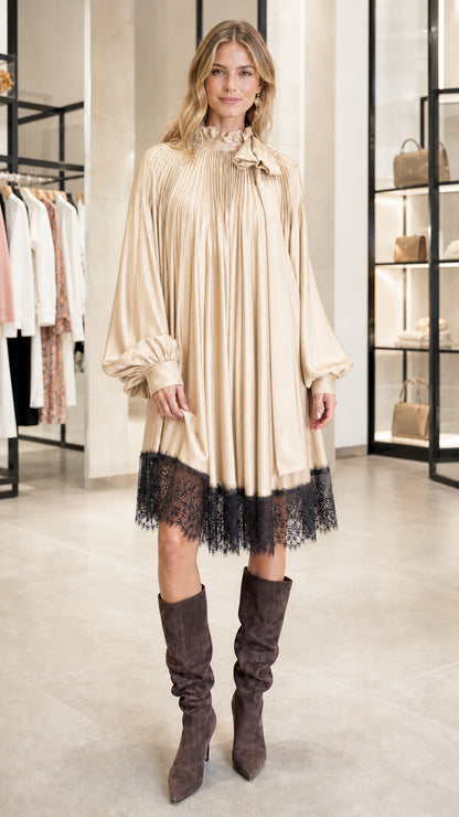 Model wearing champagne pleated satin dress with lace hem