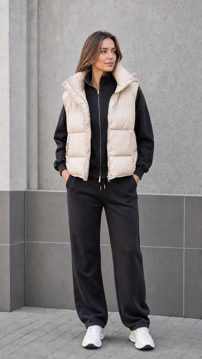 Front view of woman wearing cream beige hooded puffer vest with black sweatsuit