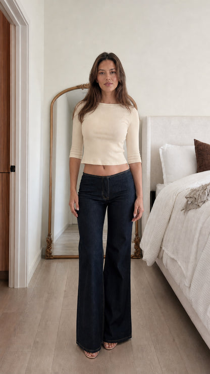 Front view of woman wearing beige ribbed cropped top and dark denim jeans